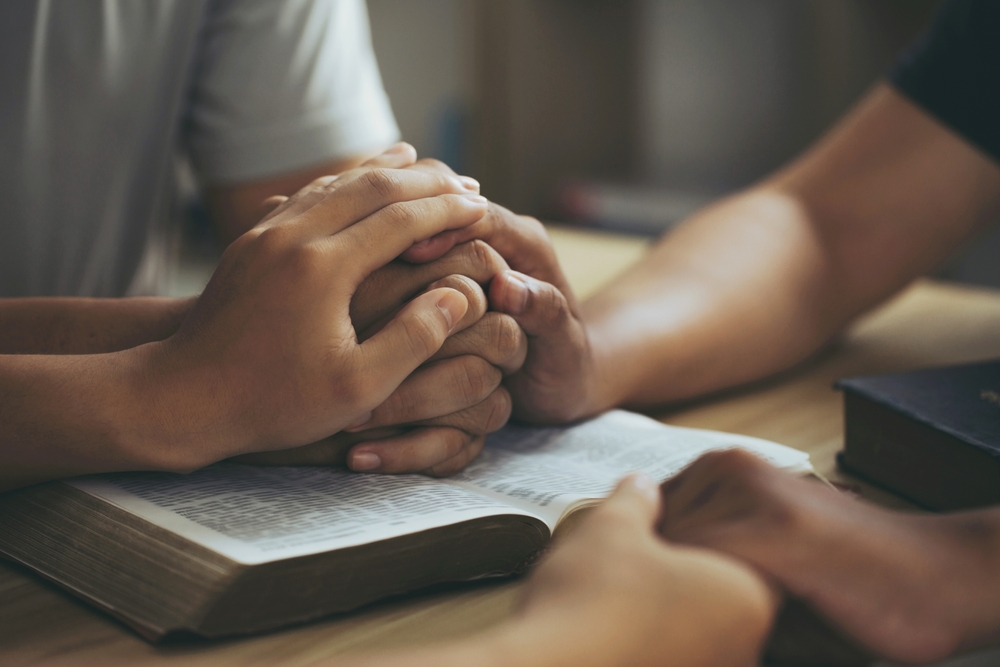 Several people hold hands over an open Bible.