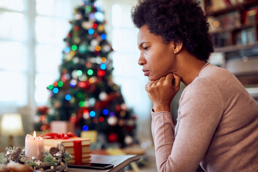 A woman sits pensively in front of a Christmas tree. 