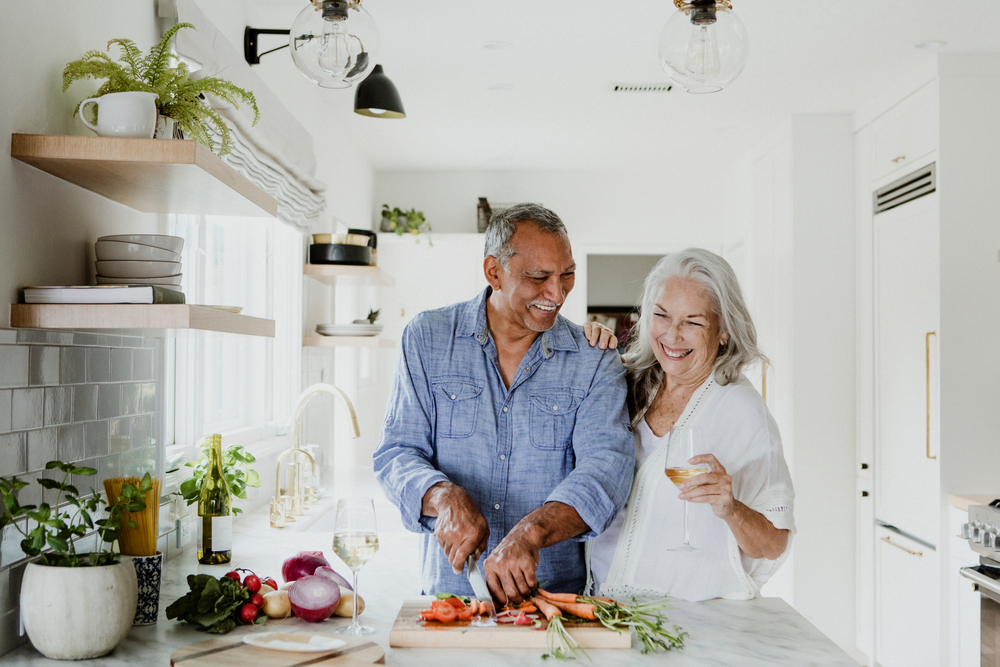 An older couple laughs as they prepare dinner together. 