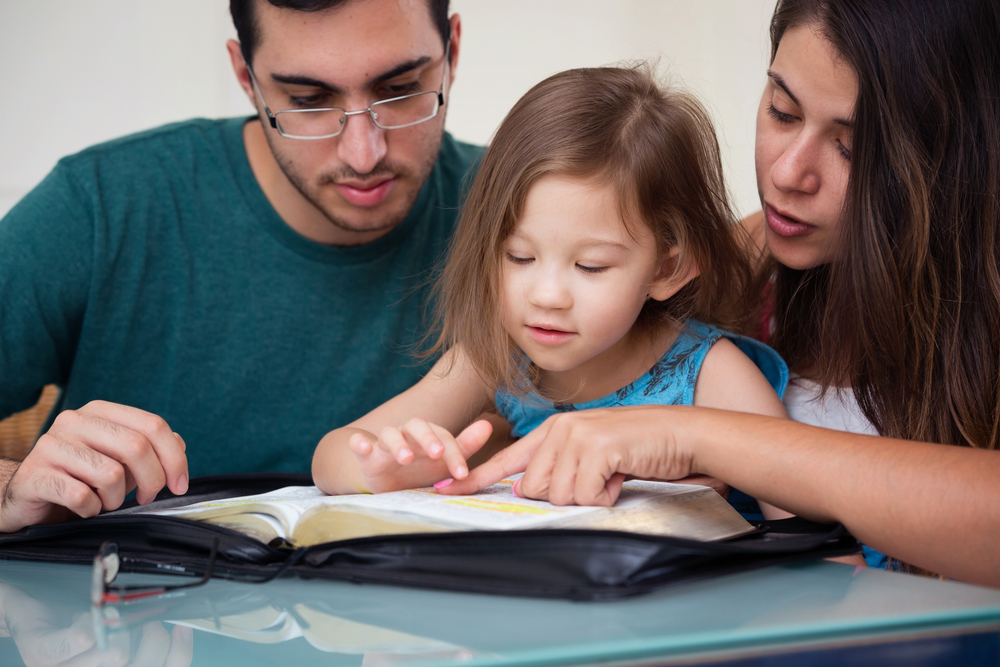 Young parents read the Bible with their daughter.