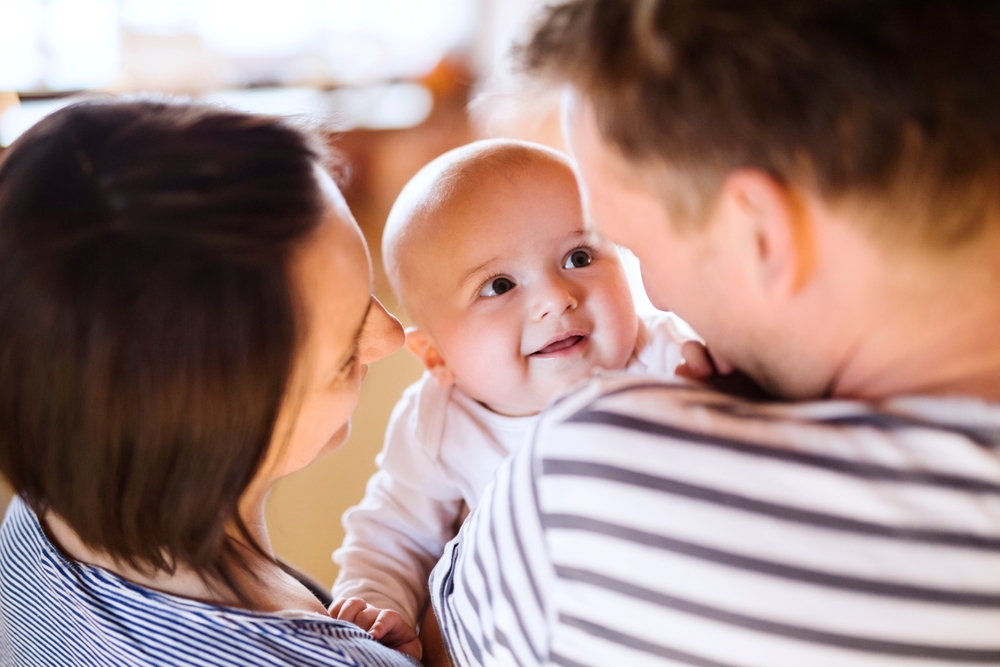 A baby smiles at its parents.