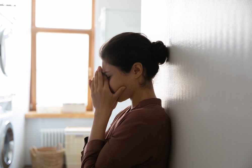 A woman sits against the wall and covers her face.